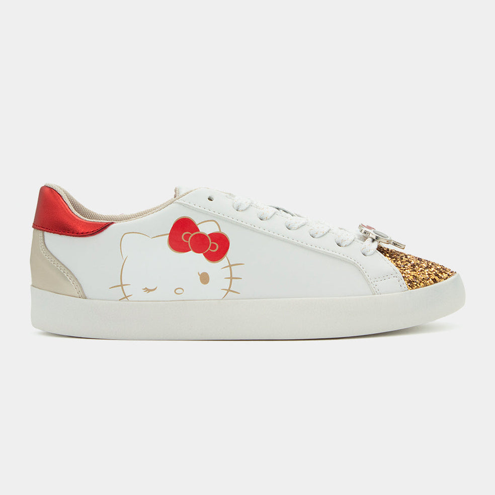 Tenis blancos Hello Kitty edición 50 aniversario con punta dorada de glitter y detalles rojos metálicos.