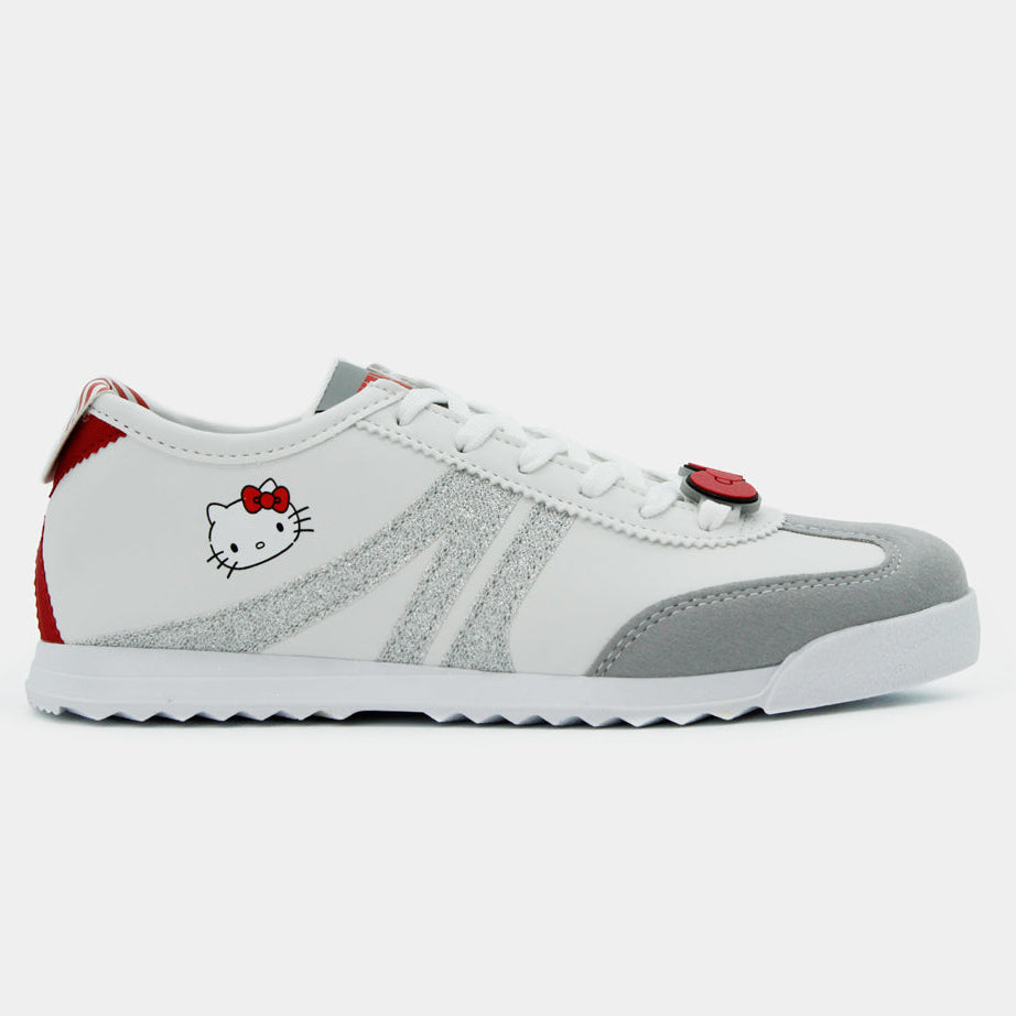 Tenis blancos Hello Kitty con franjas plateadas, suela gris dentada y pin de moño rojo en las agujetas.